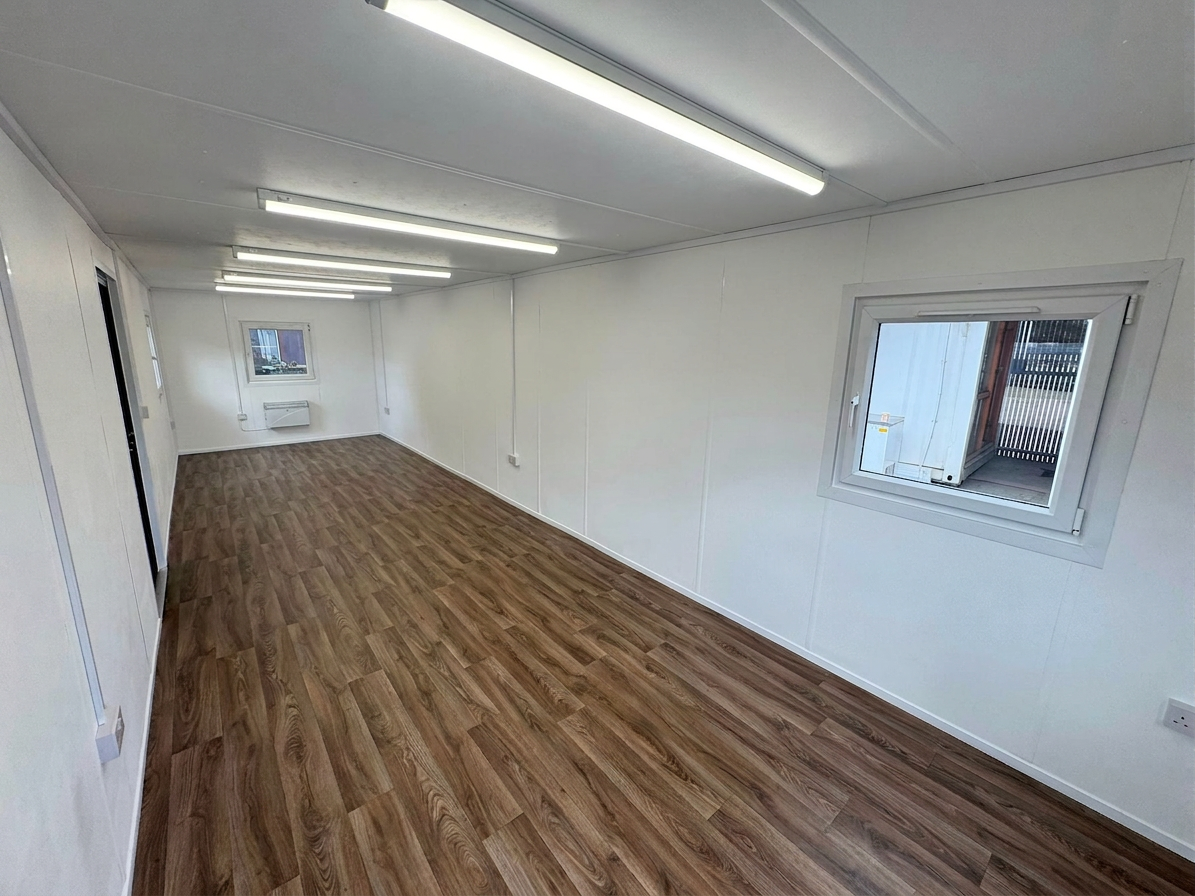 Interior of a refurbished 32ft open plan portable office cabin with wood vinyl flooring and white walls