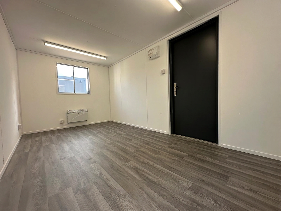 Interior of a refurbished 16x9 portable office with white walls, wood-look flooring, electric heater, and black door
