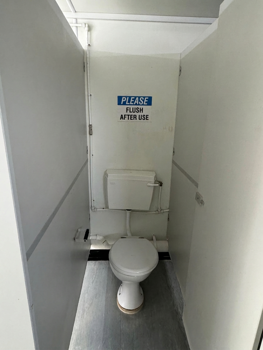 Interior view of a toilet stall inside a 21ft portable cabin with white walls and a please flush after use sign