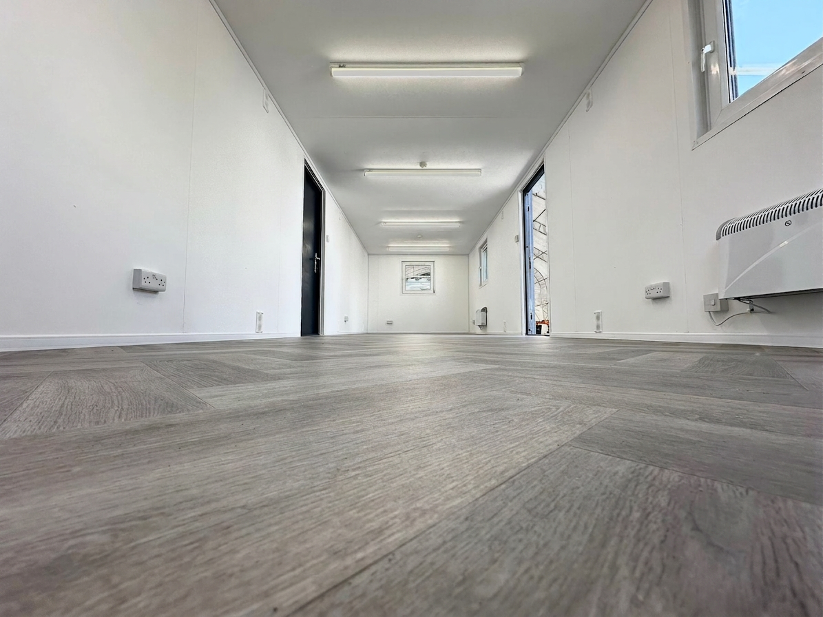 Interior of a refurbished 32x10ft portable office cabin with white walls, wood-style flooring, and LED lighting