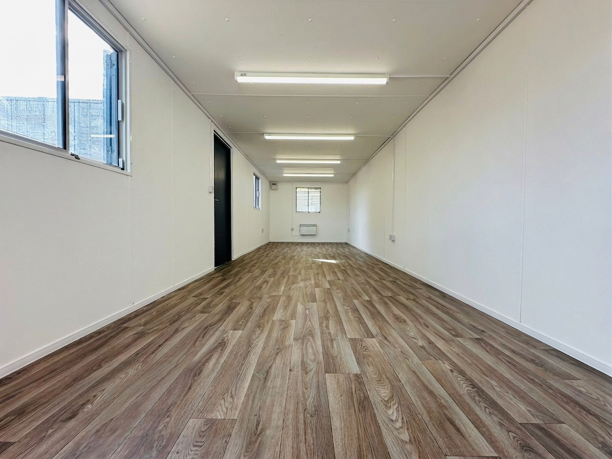 Interior view of a refurbished 32ft office container with wood-style flooring and white paneled walls