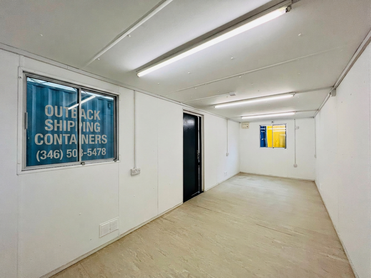 Interior of a refurbished 24x9 ft container office with white walls, fluorescent lighting, and two windows
