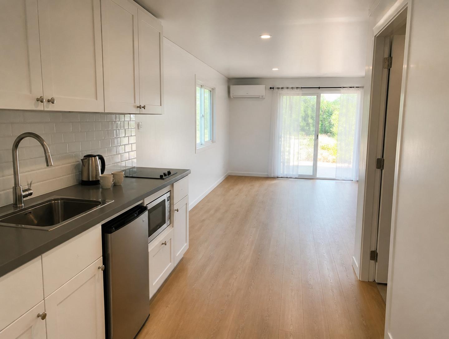 Luxury 40ft prefab container house interior — wide kitchenette with white shaker cabinets, quartz counter, stainless bar fridge and induction cooktop