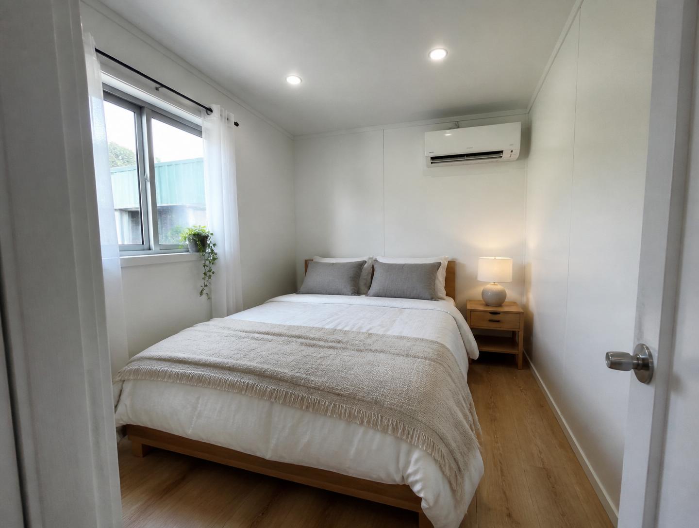 Luxury 40ft prefab container house interior — bedroom with queen bed, light-wood nightstand, ceramic lamp and mini-split HVAC